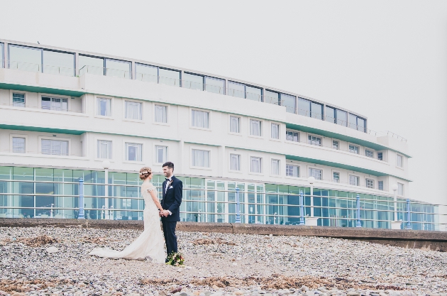 Lancashire hotel, The Midland where a bride and groom are standing on a pebble beach with the hotel in the background