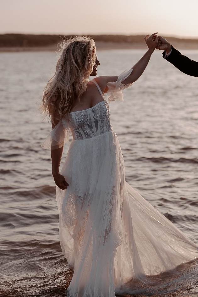 Bride walks through the waves at dusk