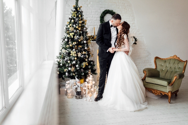 Bride and groom kiss in front of Christmas tree