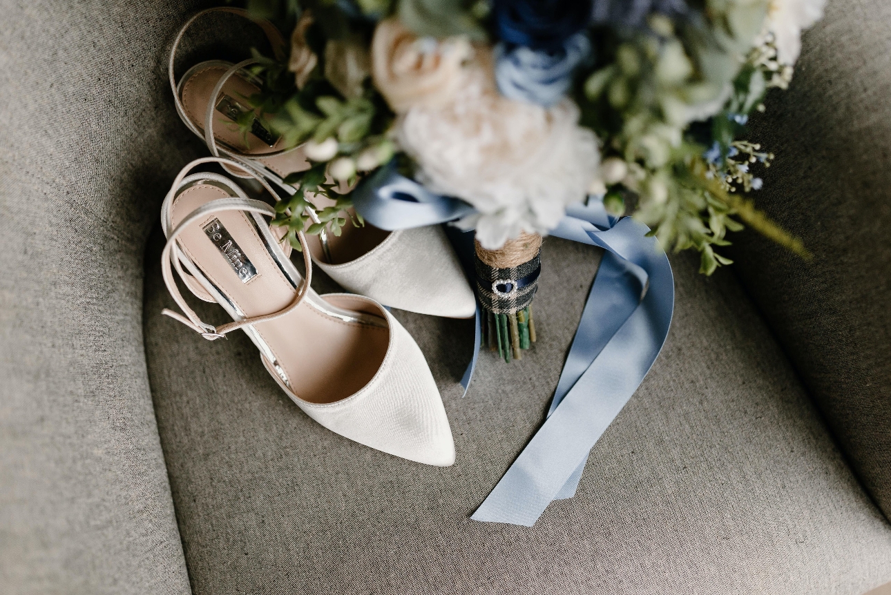 pair of wedding shoes on a grey chair with a bouquet next to it