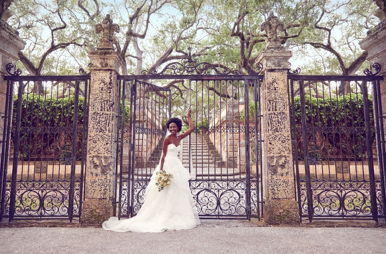model in front of black iron gates, wearing romantic layered netted dress holding bouqet
