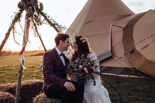 Bride and groom sitting in front of a tipi