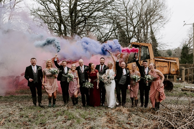 Bride and groom with their wedding party in a field holding smoke flares