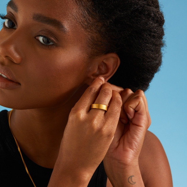 model wearing gold ring while putting in earring