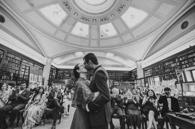 A black and white image of a bride and groom kissing in front of their friends and family