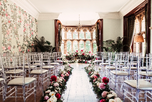 A grand bay window surrounding by pink and red flowers and chairs ready for a ceremony