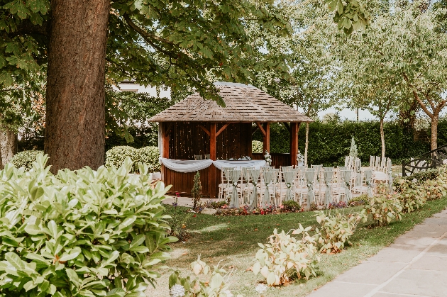 A gazebo surrounded by beautiful trees and chairs with green sashes