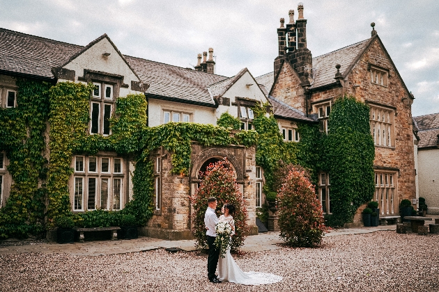 A bride and groom standing in front of a large manor house