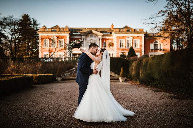A bride and groom kissing in front of a large orange building