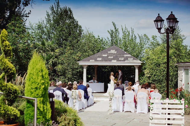 A couple getting married underneath an outdoor gazebo surrounded by friends and family