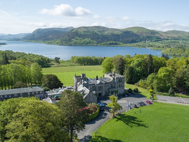 A birds eye view of a grand manor house surrounded by a lake and countryside