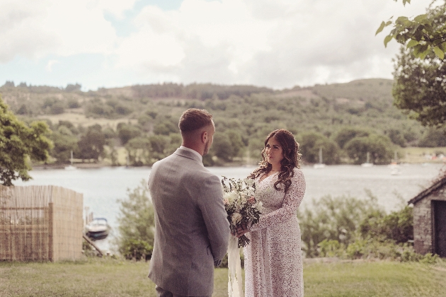 A bride and groom smiling at each other in front of a lake