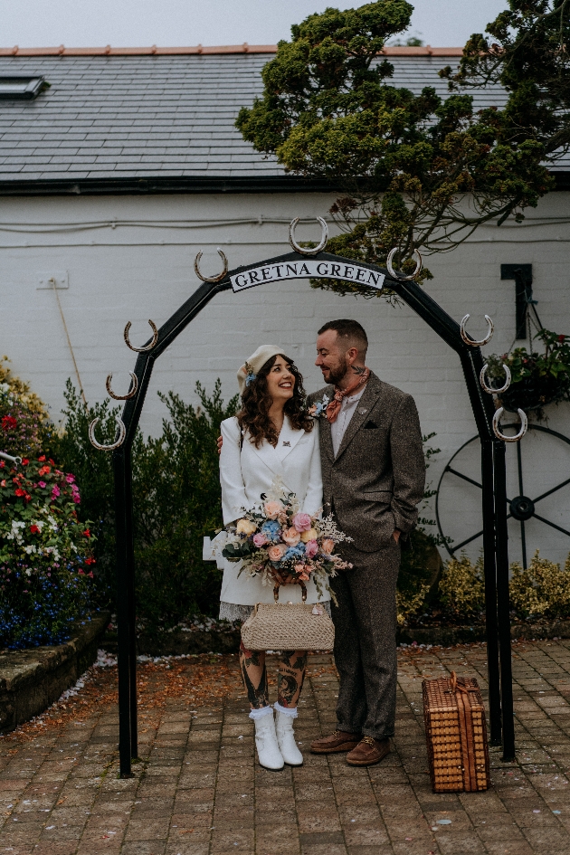A bride and groom standing underneath a sign that says Gretna Green