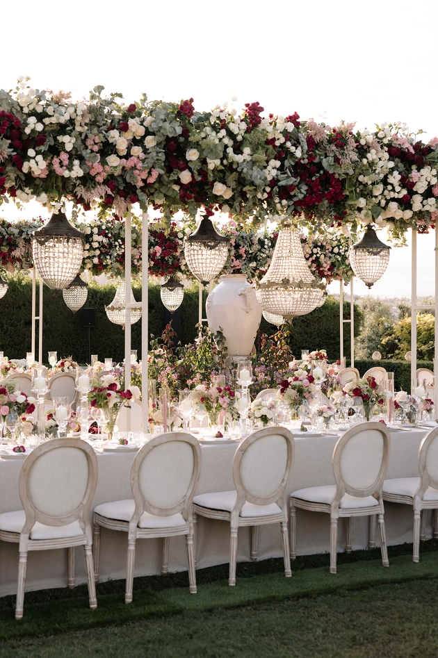 outside wedding reception with extravagant floral displays and chandeliers above table