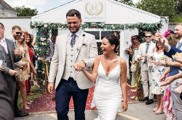 A bride and groom walking down an aisle while their friends and family throw confetti