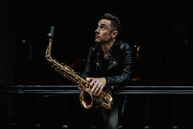 A man dressed in black looking off into the distance while holding a saxophone