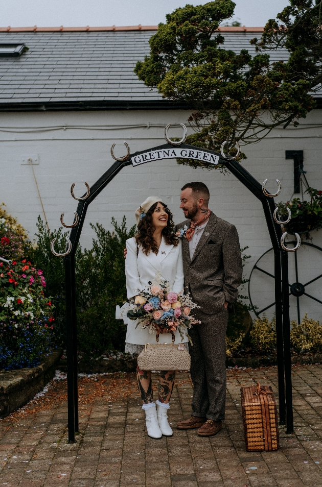 A bride and groom standing under a sign that says Gretna Green