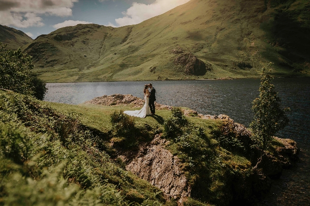 A bride and groom kissing surrounded by hills and a lake