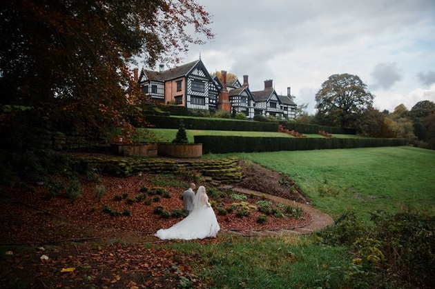 A bride and groom walking in the grounds of a manor house which can be seen in the distance