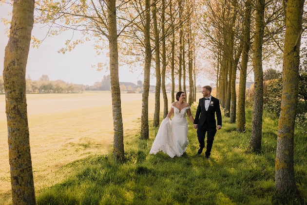 A bride and groom walking hand-in-hand in the woods