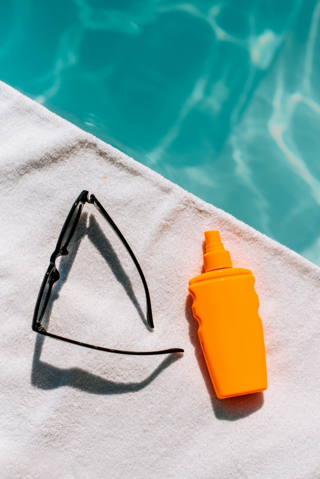 Orange bottle and black sunglasses on white towel next to pool 
