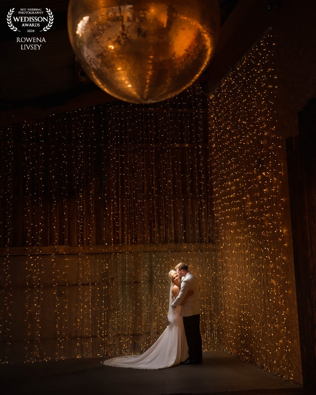 A bride and groom standing underneath a disco wall surrounded by fairylights