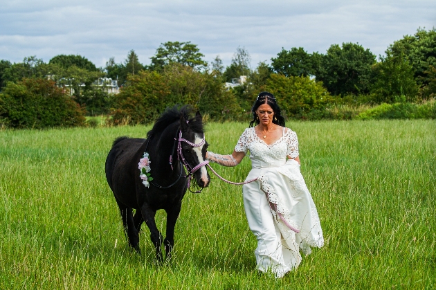 A bride walking through a field with a horse
