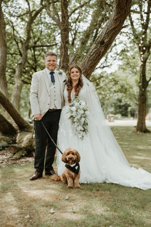 A bride and groom posing with a dog